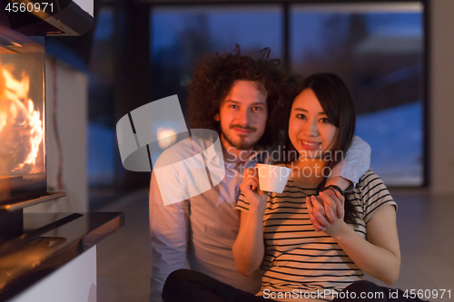 Image of happy multiethnic couple sitting in front of fireplace