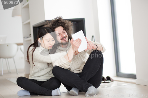 Image of multiethnic couple using tablet computer in front of fireplace