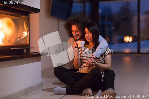 Image of happy multiethnic couple sitting in front of fireplace