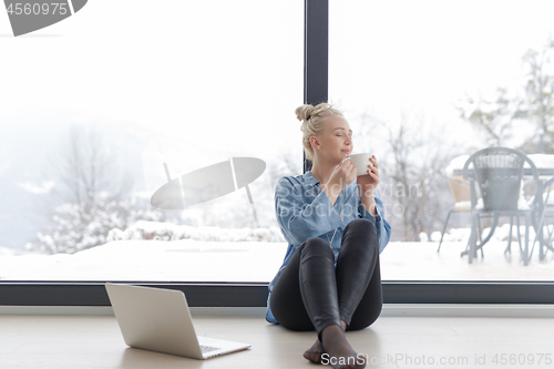 Image of woman drinking coffee and using laptop at home