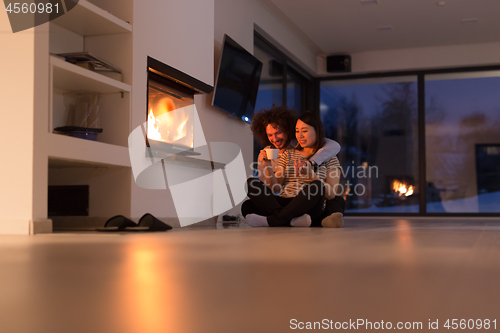 Image of happy multiethnic couple sitting in front of fireplace