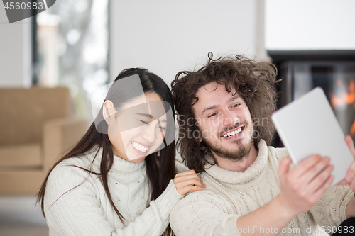 Image of multiethnic couple using tablet computer in front of fireplace