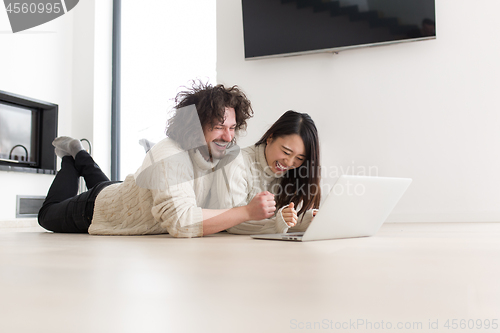 Image of young multiethnic couple using a laptop on the floor