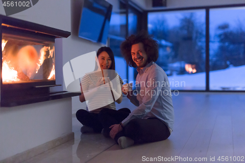 Image of happy multiethnic couple sitting in front of fireplace