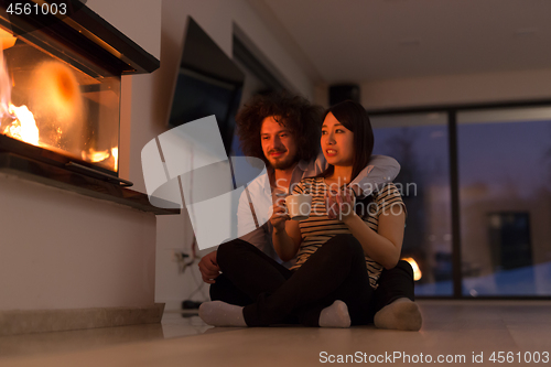 Image of happy multiethnic couple sitting in front of fireplace