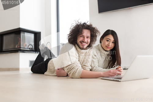 Image of young multiethnic couple using a laptop on the floor