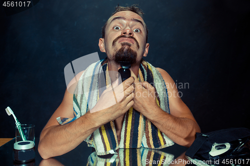 Image of young man in bedroom sitting in front of the mirror scratching his beard