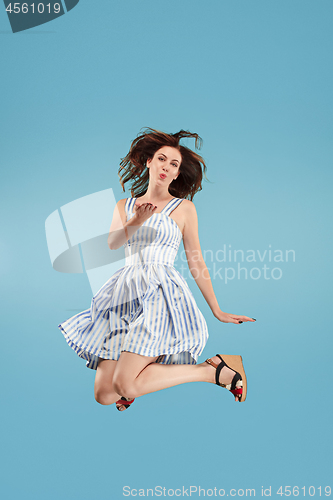 Image of Freedom in moving. Pretty young woman jumping against blue background