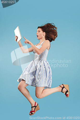 Image of Image of young woman over blue background using laptop computer or tablet gadget while jumping.