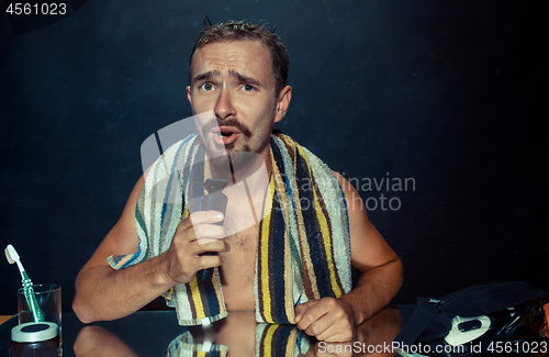 Image of young man in bedroom sitting in front of the mirror scratching his beard