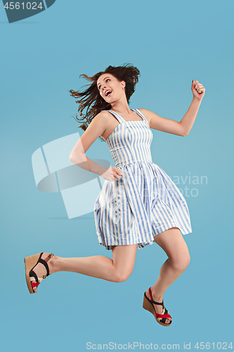 Image of Freedom in moving. Pretty young woman jumping against blue background