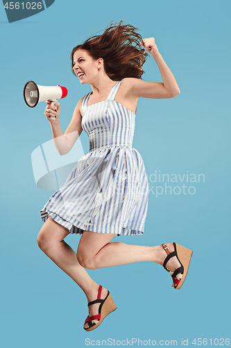 Image of Beautiful young woman jumping with megaphone isolated over blue background