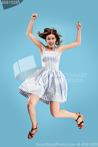 Image of Freedom in moving. Pretty young woman jumping against blue background