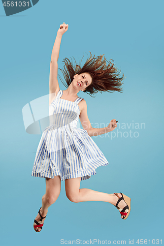 Image of Freedom in moving. Pretty young woman jumping against blue background