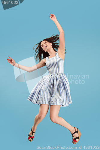 Image of Freedom in moving. Pretty young woman jumping against blue background