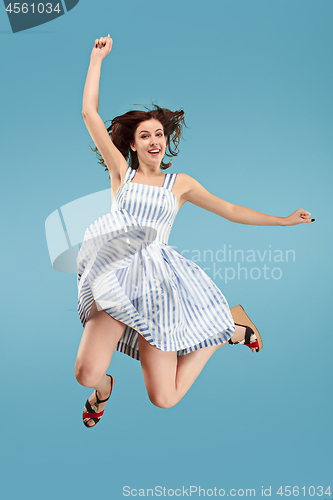 Image of Freedom in moving. Pretty young woman jumping against blue background