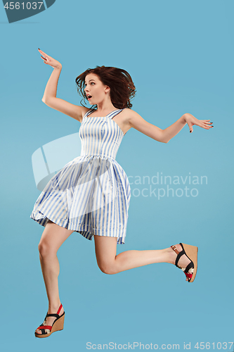 Image of Freedom in moving. Pretty young woman jumping against blue background