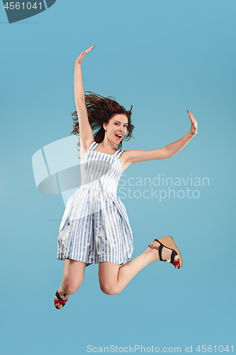 Image of Freedom in moving. Pretty young woman jumping against blue background