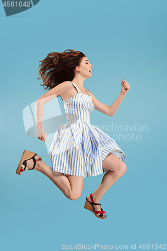 Image of Freedom in moving. Pretty young woman jumping against blue background