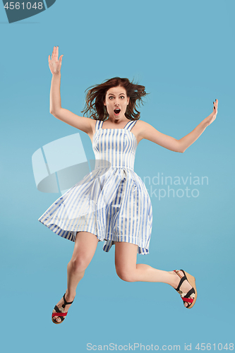 Image of Freedom in moving. Pretty young woman jumping against blue background