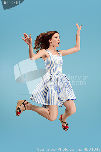 Image of Freedom in moving. Pretty young woman jumping against blue background