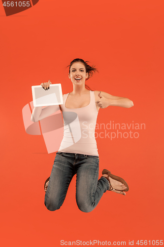 Image of Image of young woman over blue background using laptop computer or tablet gadget while jumping.