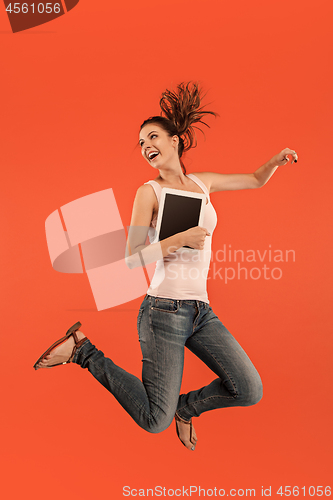 Image of Image of young woman over blue background using laptop computer or tablet gadget while jumping.