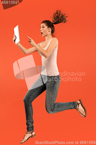 Image of Image of young woman over blue background using laptop computer or tablet gadget while jumping.