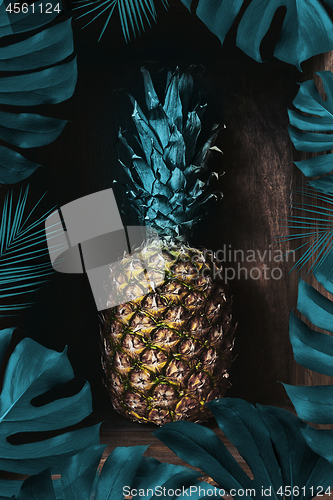 Image of Fresh pineapple on an old wooden background decorated with a frame of palm leaves. Tropical fruit