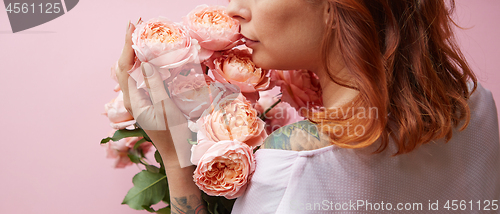 Image of Red-haired woman with tattoo on her shoulders holds delicate fresh coral roses on a living coral background. A gift for Mother\'s Day. Copy space.