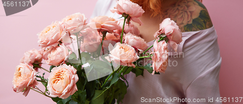 Image of Nice fresh bouquet of coral colored roses in girl\'s hand and tattoo on her shoulder on a living coral background, copy space. Gift for Mother\'s Day