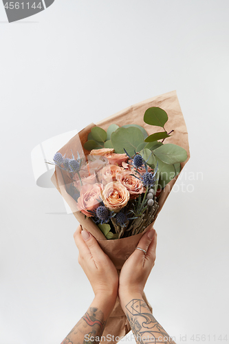 Image of Woman\'s hands hold colourful blossoming flower bouquet of fresh roses living coral color on a gray background. Copy space. Mother\'s and Woman\'s Day.
