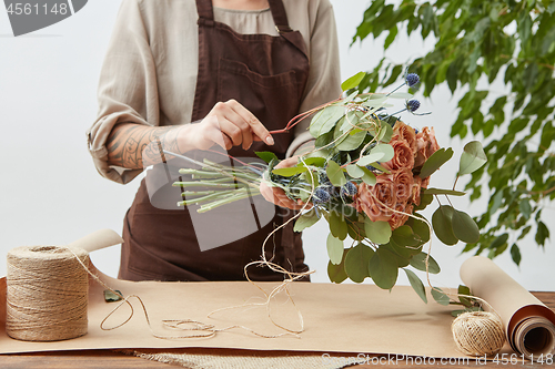 Image of Female florist is decorating beautiful bouquet from fresh natural roses step by step at the table with paper and rope on it. Mother\'s Day holiday.