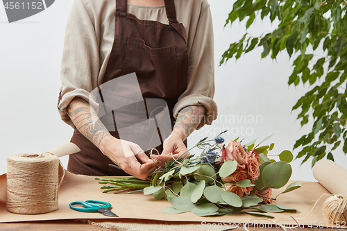 Image of Florist woman is creating fresh rose bouquet on a gray background. Process step by step. Small business with flowers delivery. Mother\'s Day.
