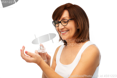 Image of smiling senior woman spraying perfume to her wrist