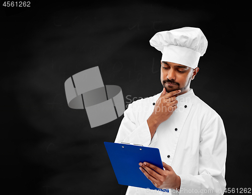 Image of chef reading menu on clipboard over chalkboard