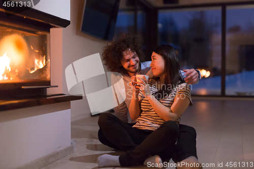 Image of happy multiethnic couple sitting in front of fireplace