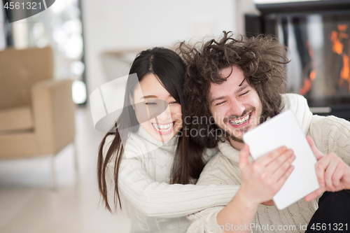 Image of multiethnic couple using tablet computer in front of fireplace