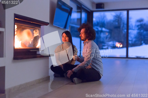 Image of happy multiethnic couple sitting in front of fireplace