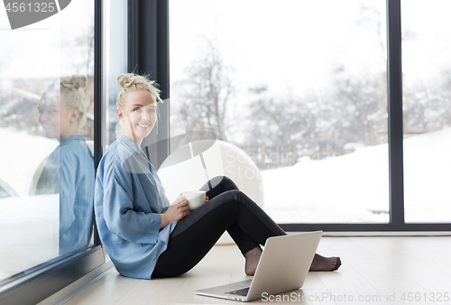 Image of woman drinking coffee and using laptop at home