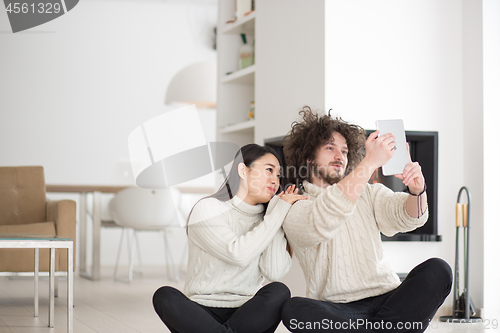 Image of multiethnic couple using tablet computer in front of fireplace