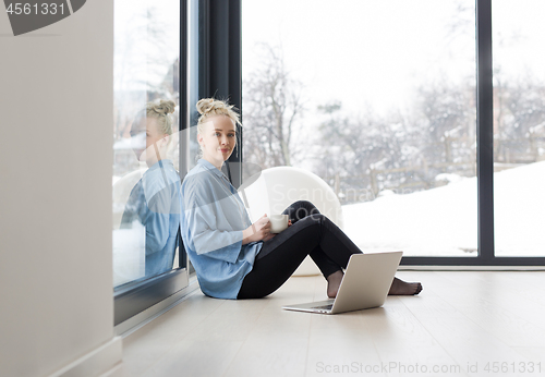 Image of woman drinking coffee and using laptop at home