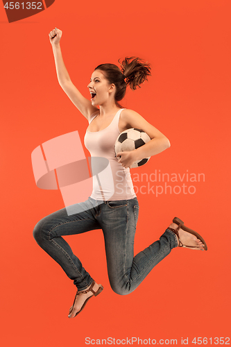 Image of Forward to the victory.The young woman as soccer football player jumping and kicking the ball at studio on a red