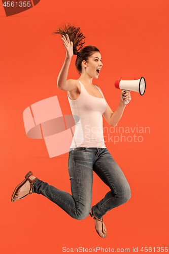 Image of Beautiful young woman jumping with megaphone isolated over red background