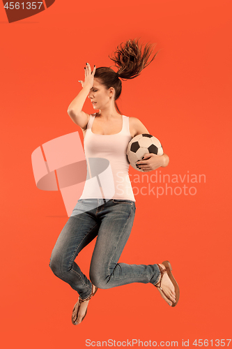 Image of Forward to the victory.The young woman as soccer football player jumping and kicking the ball at studio on a red