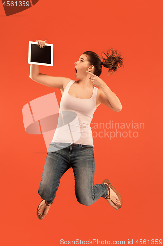 Image of Image of young woman over blue background using laptop computer or tablet gadget while jumping.