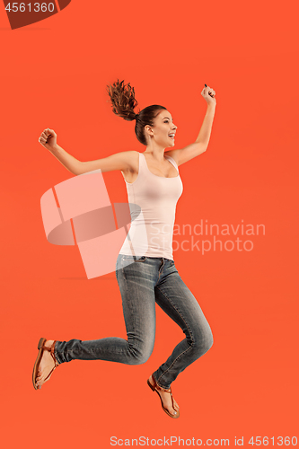 Image of Freedom in moving. Pretty young woman jumping against orange background