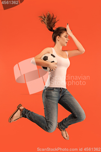 Image of Forward to the victory.The young woman as soccer football player jumping and kicking the ball at studio on a red