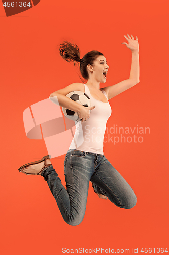 Image of Forward to the victory.The young woman as soccer football player jumping and kicking the ball at studio on a red