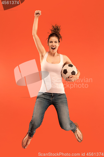 Image of Forward to the victory.The young woman as soccer football player jumping and kicking the ball at studio on a red